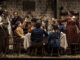The Cratchits toast to Scrooge while he looks on